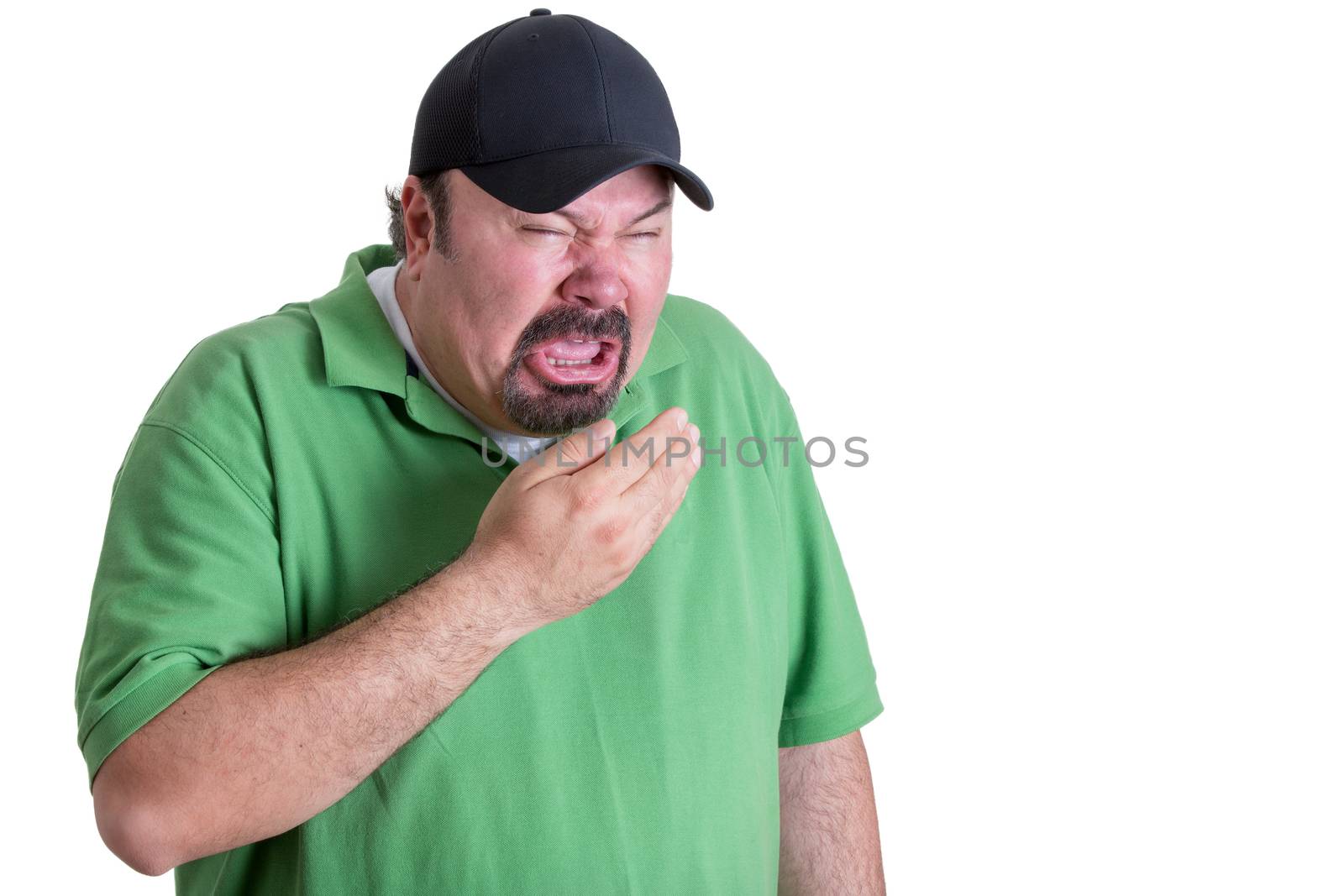 Upper Body Image of Overweight Man Wearing Green Shirt and Black Baseball Cap Covering Mouth While Sneezing in front of White Background