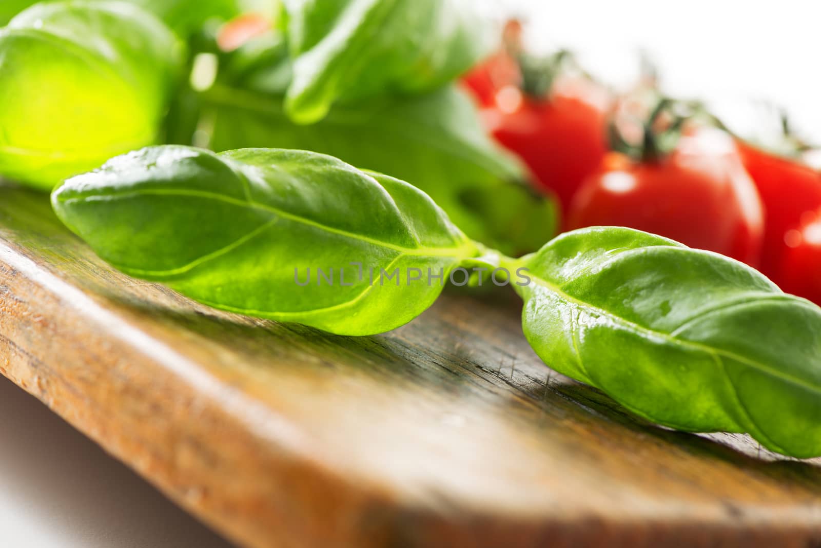 Tomatoes and basil leaf on wooden table by Nanisimova