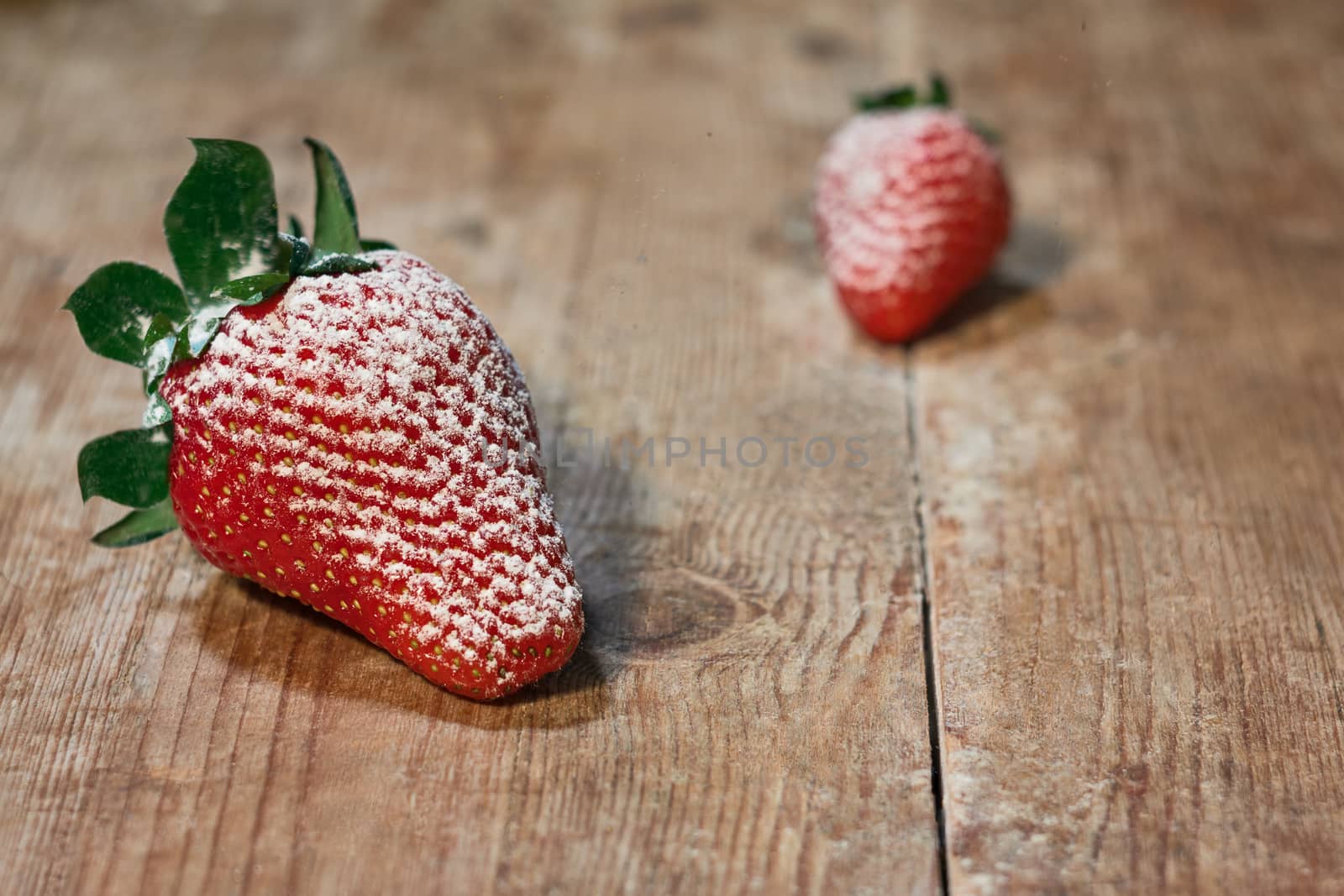 Red strawberries sprinkled with sugar on a wooden table