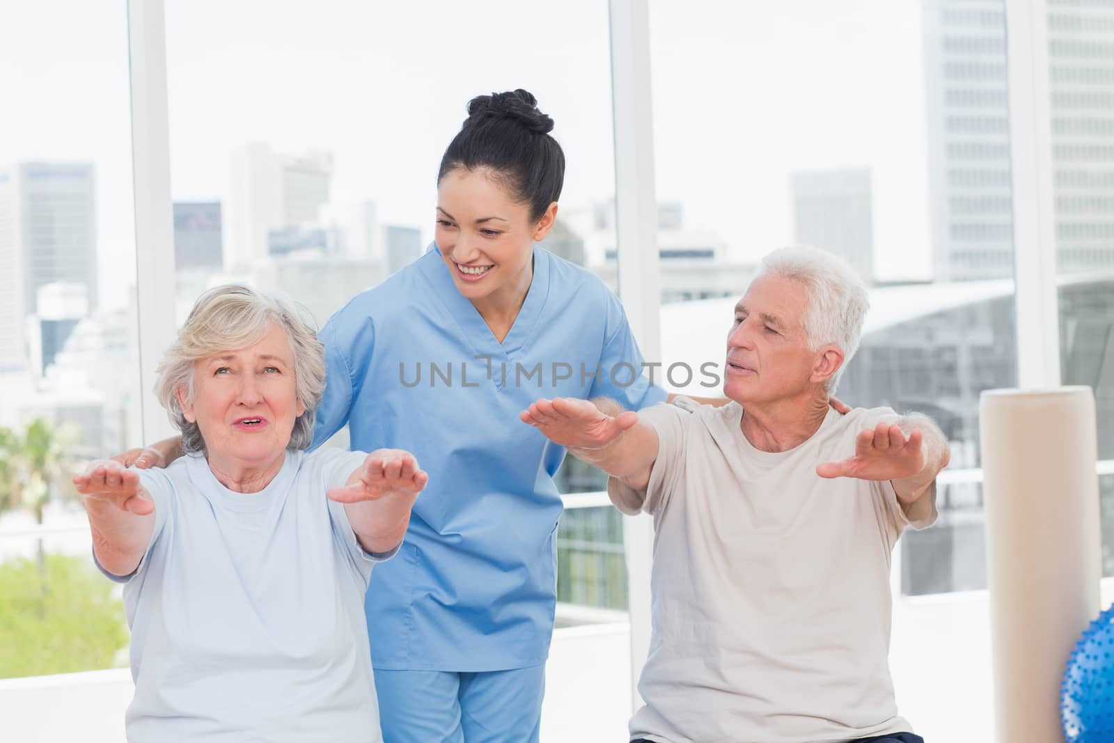Happy trainer assisting senior couple to exercise in gym