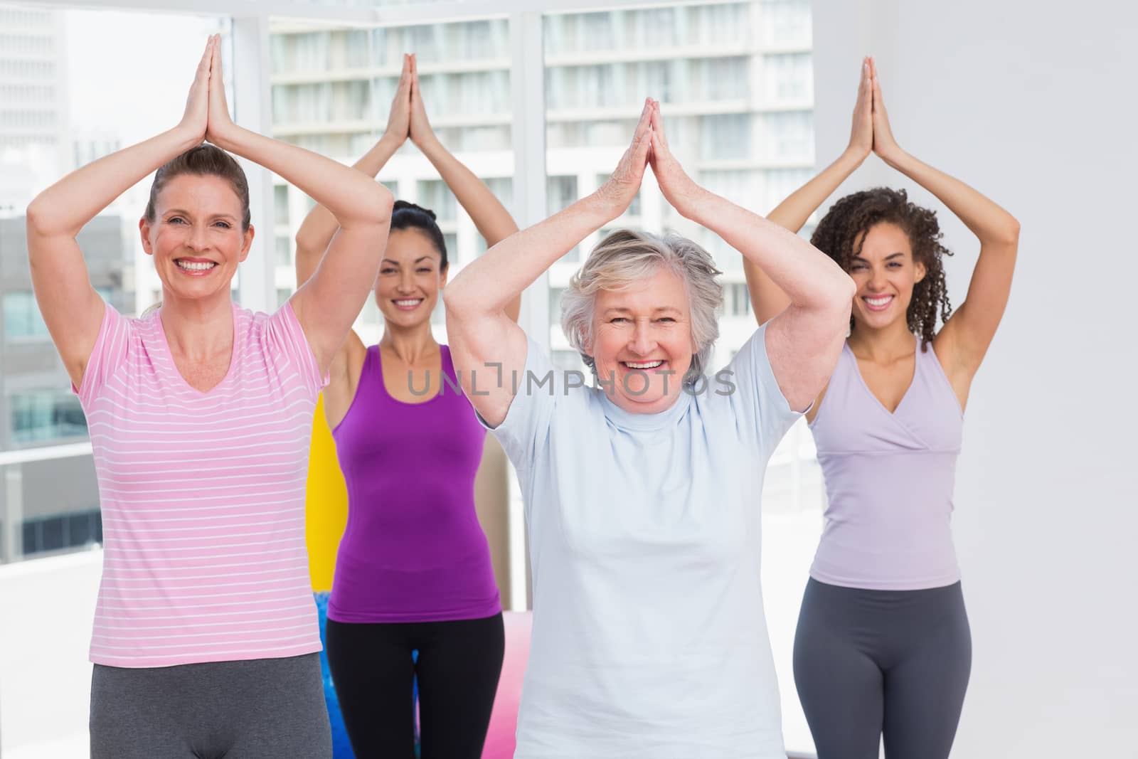 Portrait of happy female friend with hands clasped standing in gym