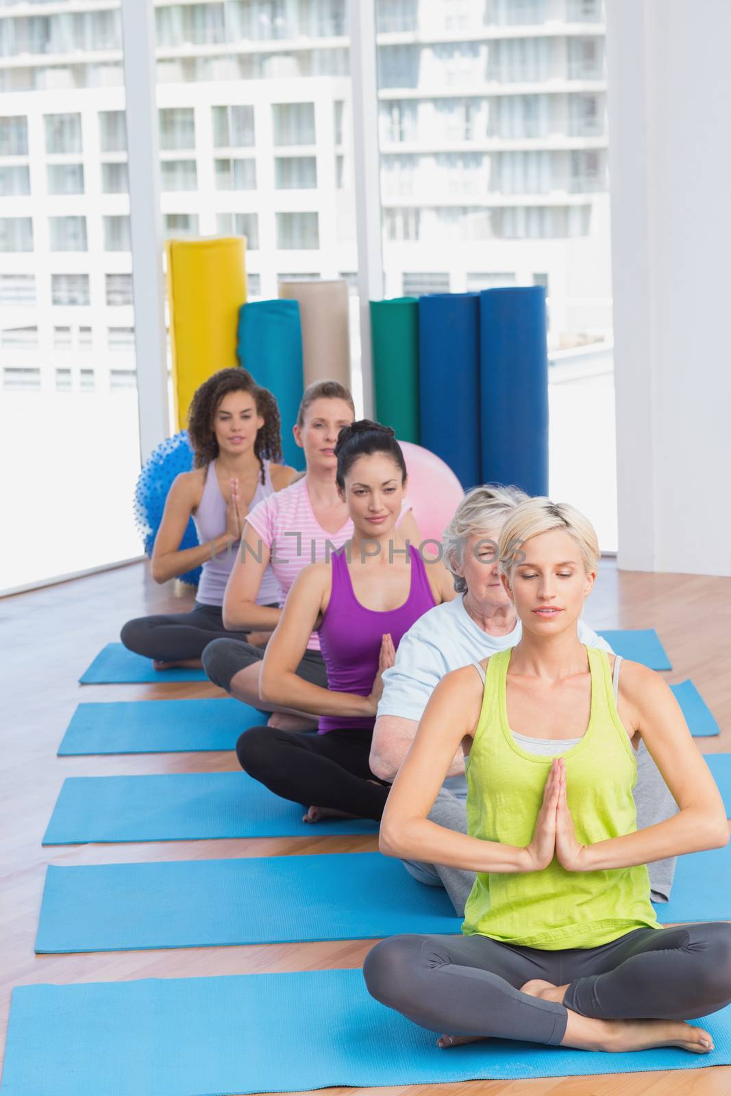 Row of fit women meditating in fitness class