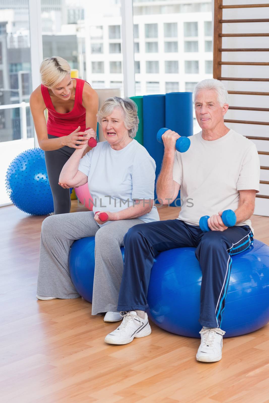 Female trainer motivating senior couple in lifting dumbbells at gym