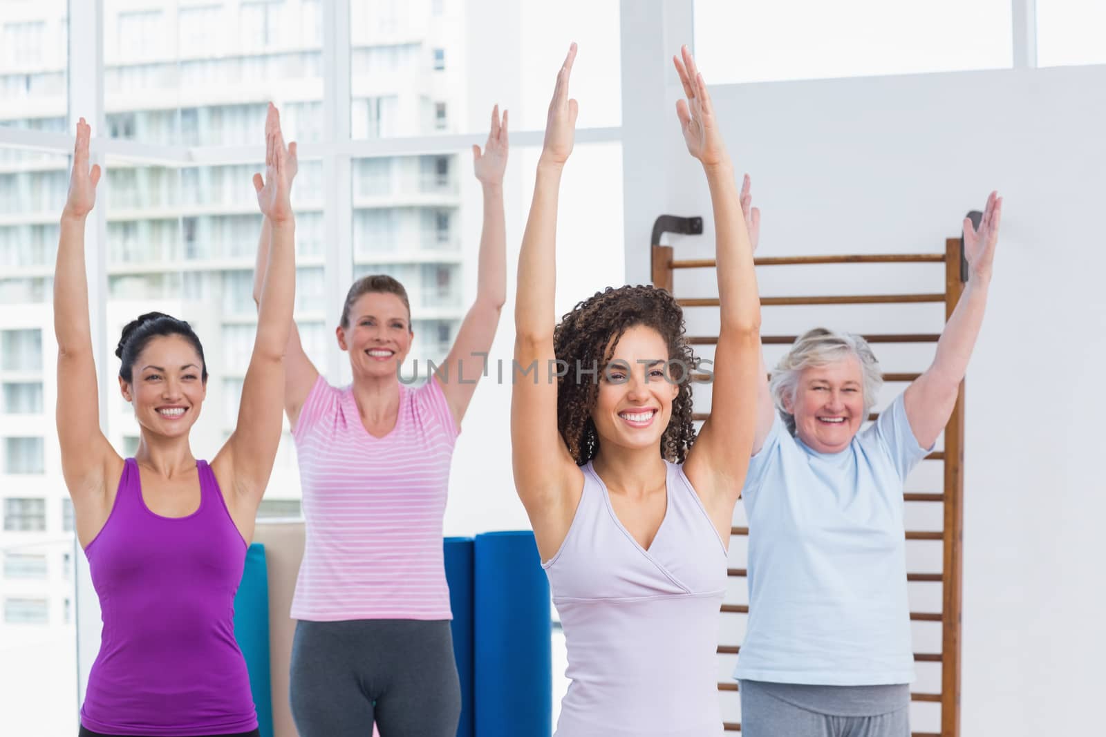 Happy female friends with arms raised exercising in gym