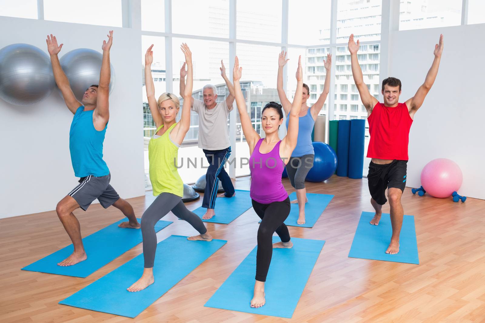 Full length of people with hands raised doing yoga at fitness club