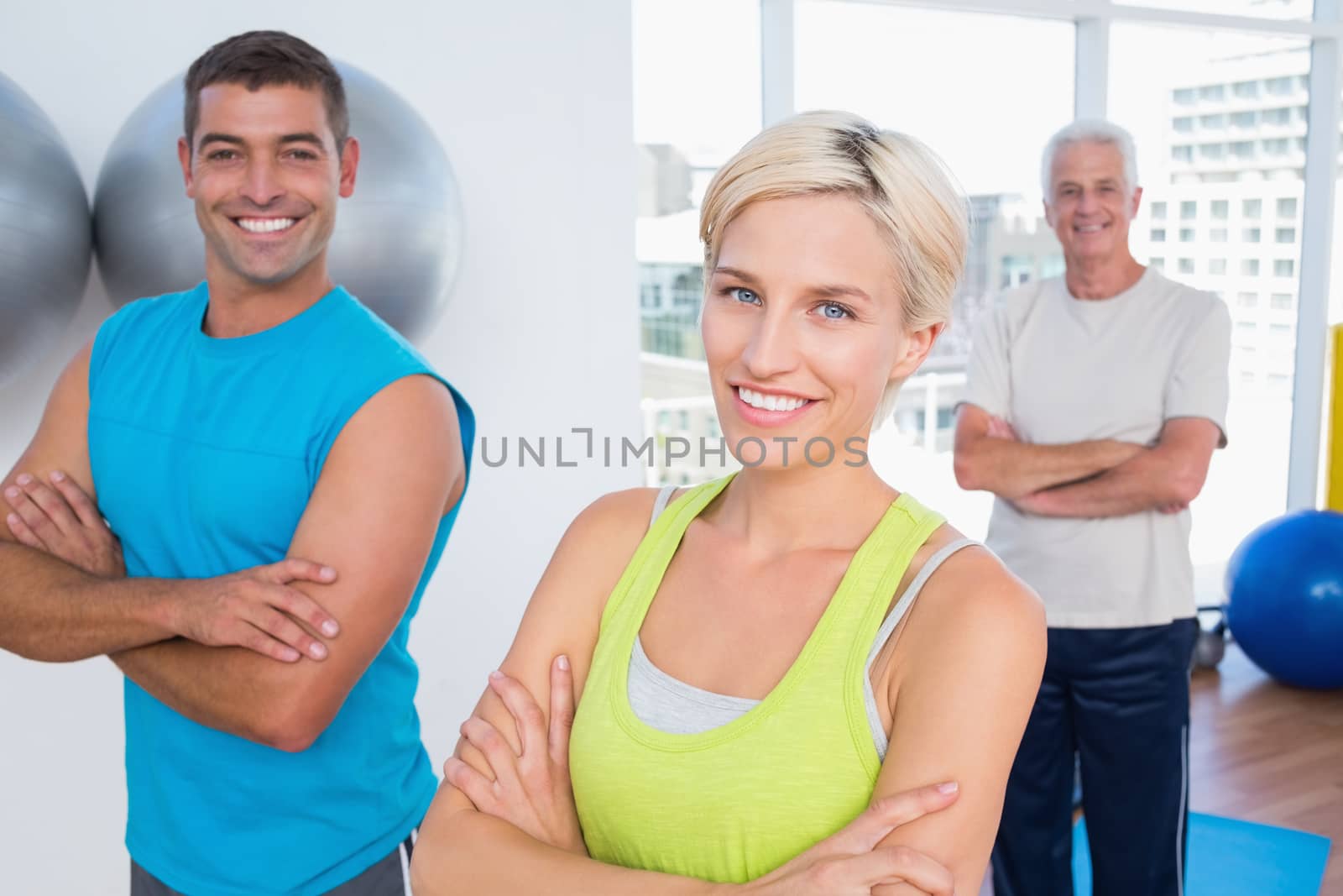 Portrait of happy woman with male friends standing arms crossed at gym class