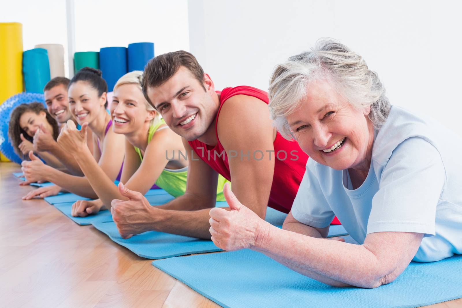 People gesturing thumbs up while lying on mats at gym by Wavebreakmedia