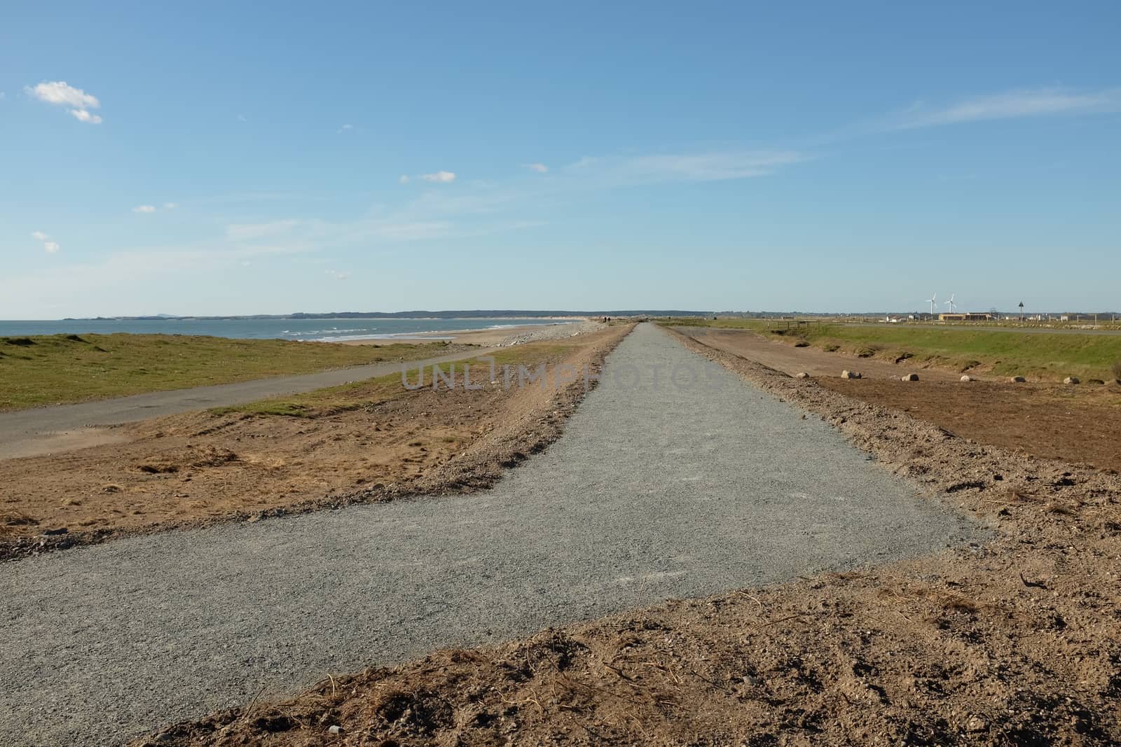 A newly layed gravel footpath on raised earth extends to the horizon with the sea in the distance.