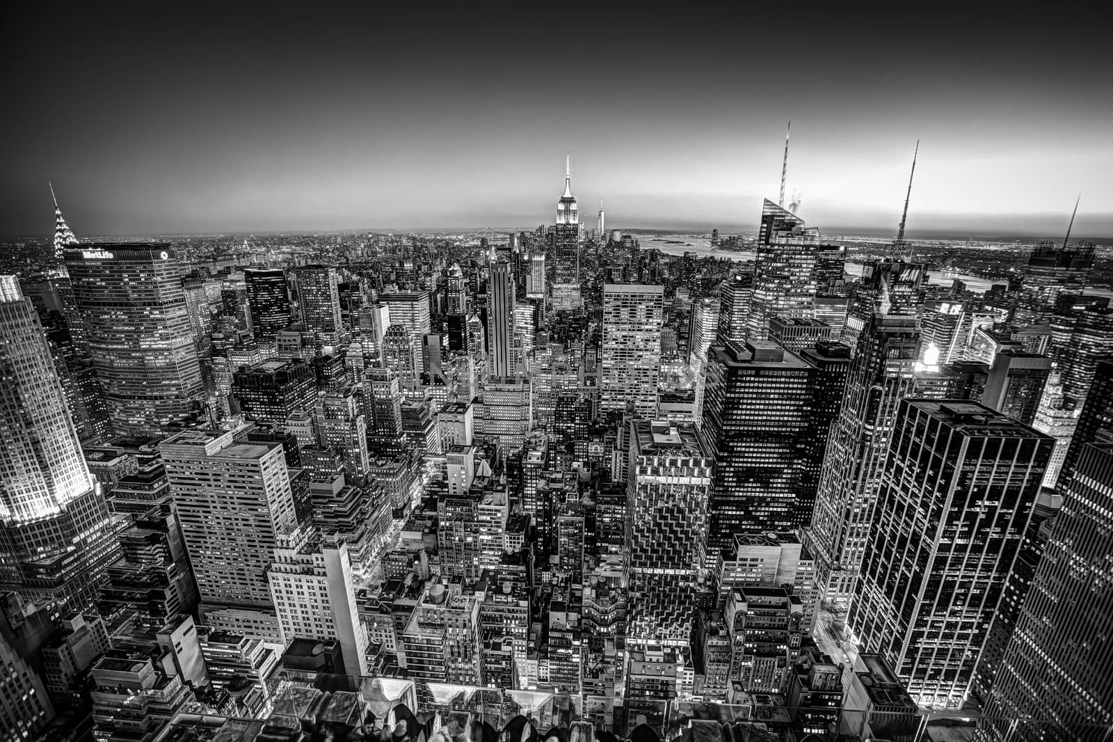 New York City. Manhattan downtown skyline with illuminated Empire State Building and skyscrapers at dusk seen from Top of the Rock observation deck. Black and white shot.