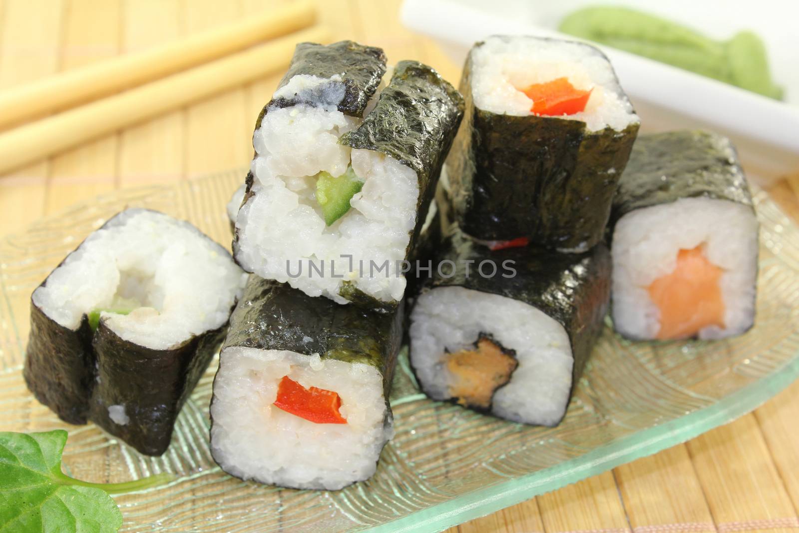 a glass bowl with sushi and wasabi leaves