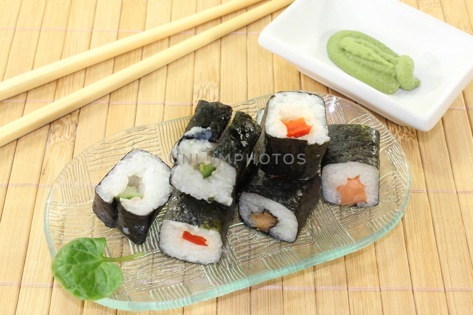 a glass bowl with sushi and wasabi leaves