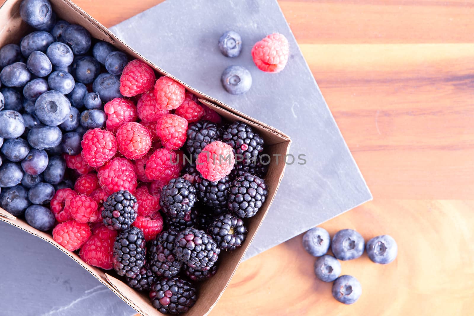 Box of fresh seasonal autumn berries with blueberries, blackberries, and raspberries displayed in a punnet on a wooden table fresh from the farmers market, with copy space