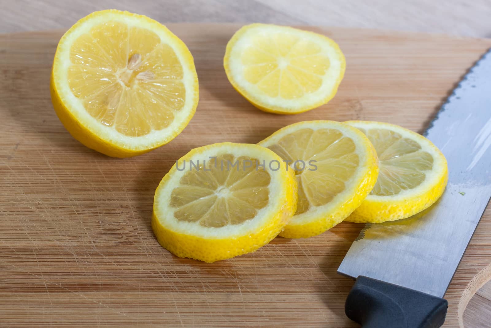 Slice lemons on a wooden cutting board with a knife and natural light streaming in from the right.