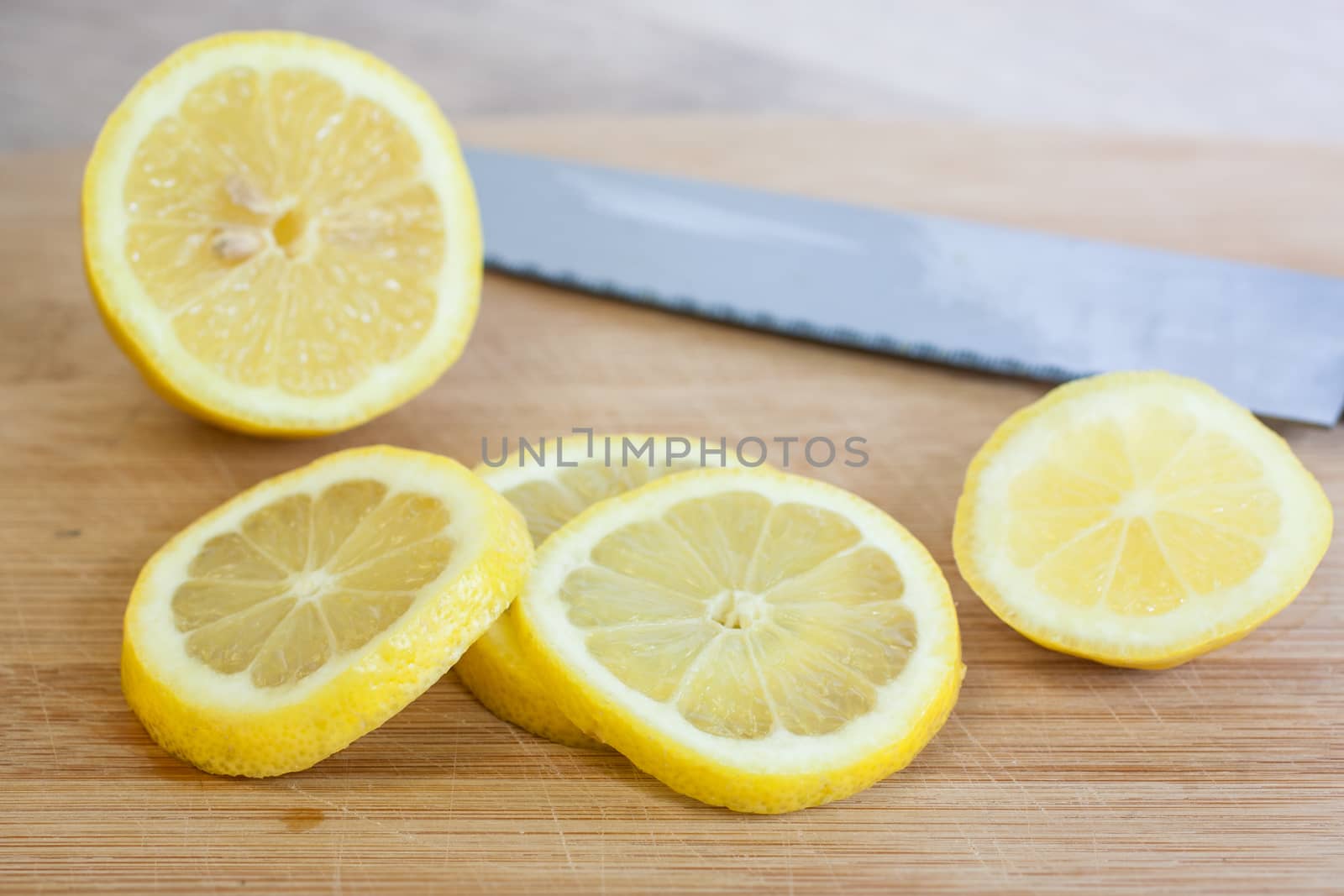 Slice lemons on a wooden cutting board with a knife and natural light streaming in from the right.