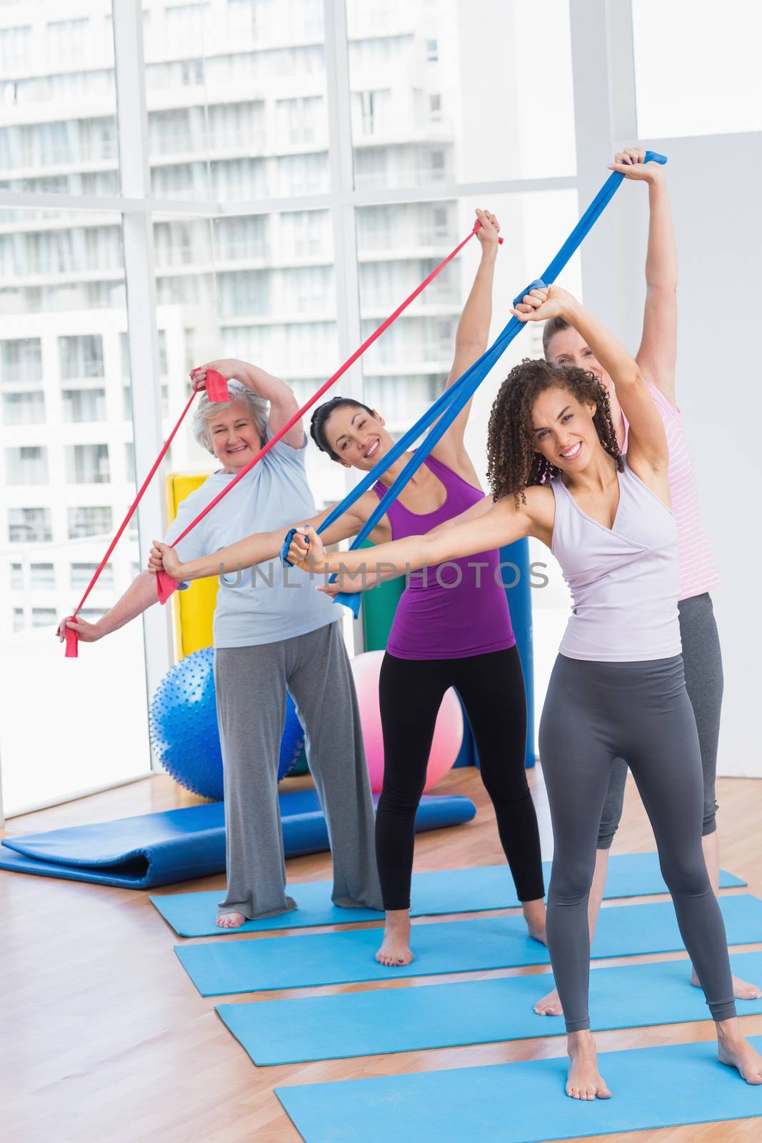 Full length portrait of happy female friends exercising with resistance bands in gym