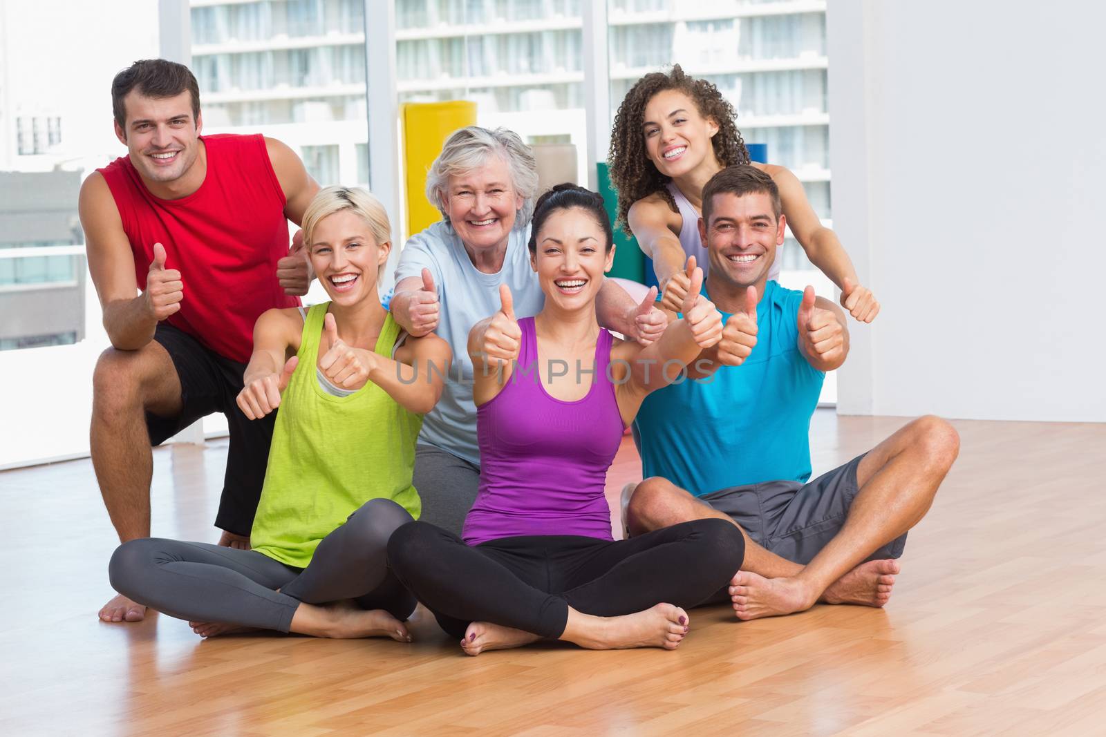 Fit men and women gesturing thumbs up in fitness studio by Wavebreakmedia