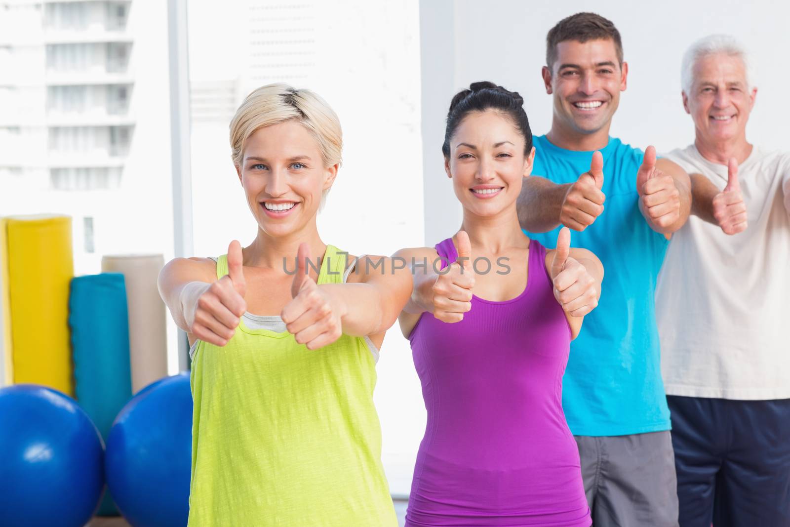Portrait of happy fit people gesturing thumbs up at gym
