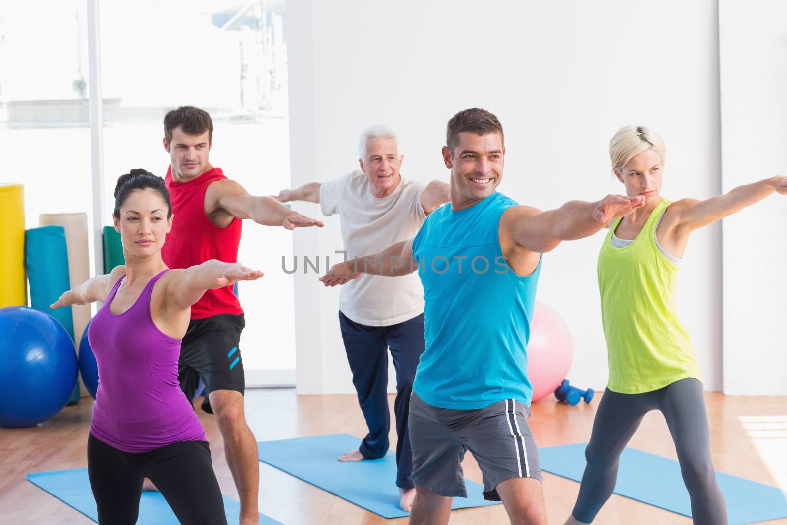 Fit men and women doing warrior pose in yoga class