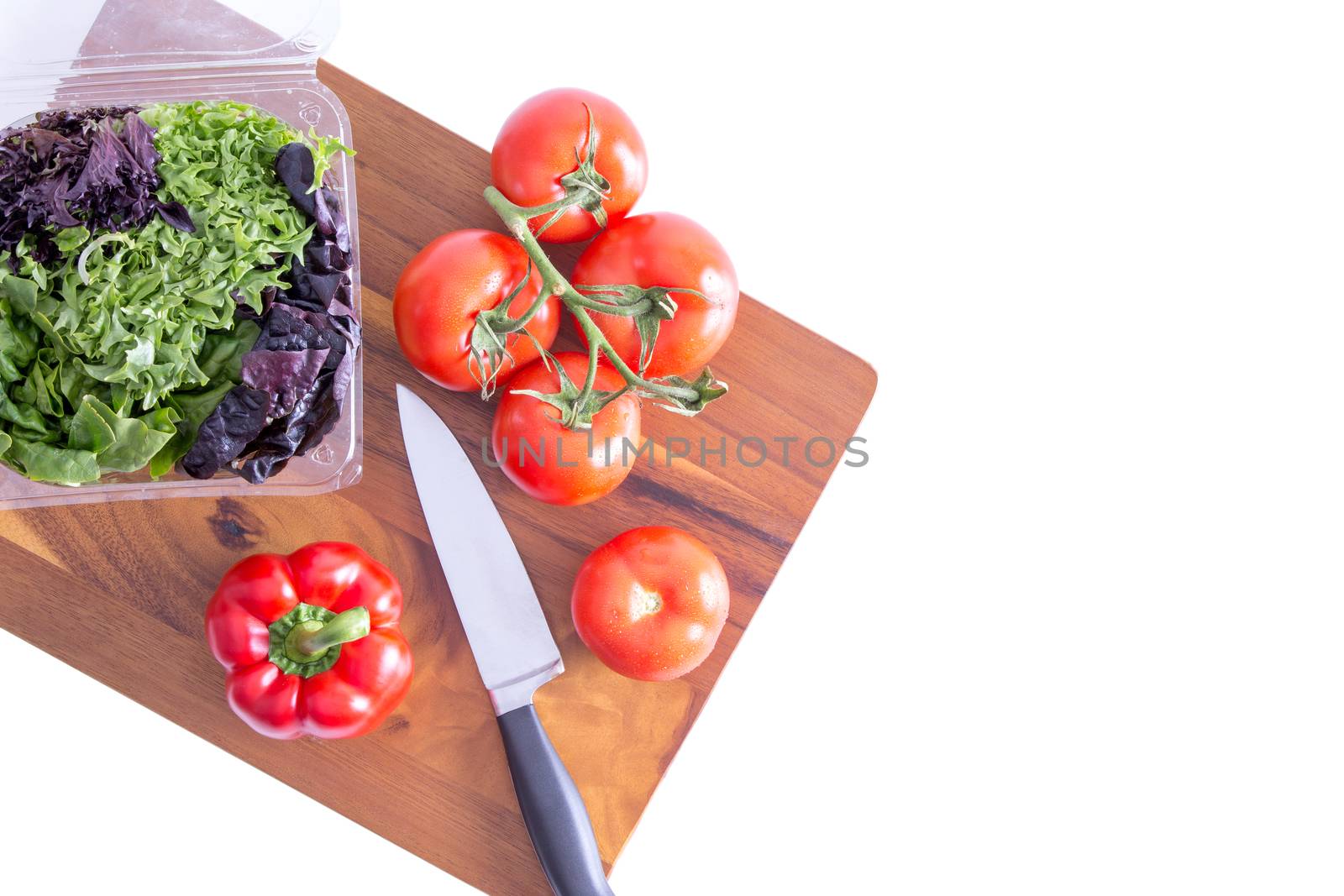 Preparing a healthy leafy green salad with farm fresh sweet bell pepper, tomatoes and assorted lettuce cultivars on a wooden chopping board with a knife, view from above on white with copyspace