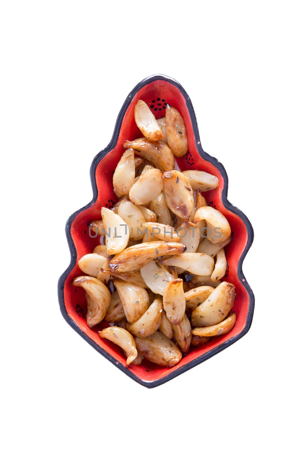 Roasted spicy marinated garlic cloves in a decorative leaf-shaped glazed pottery dish viewed from overhead centered on a white background