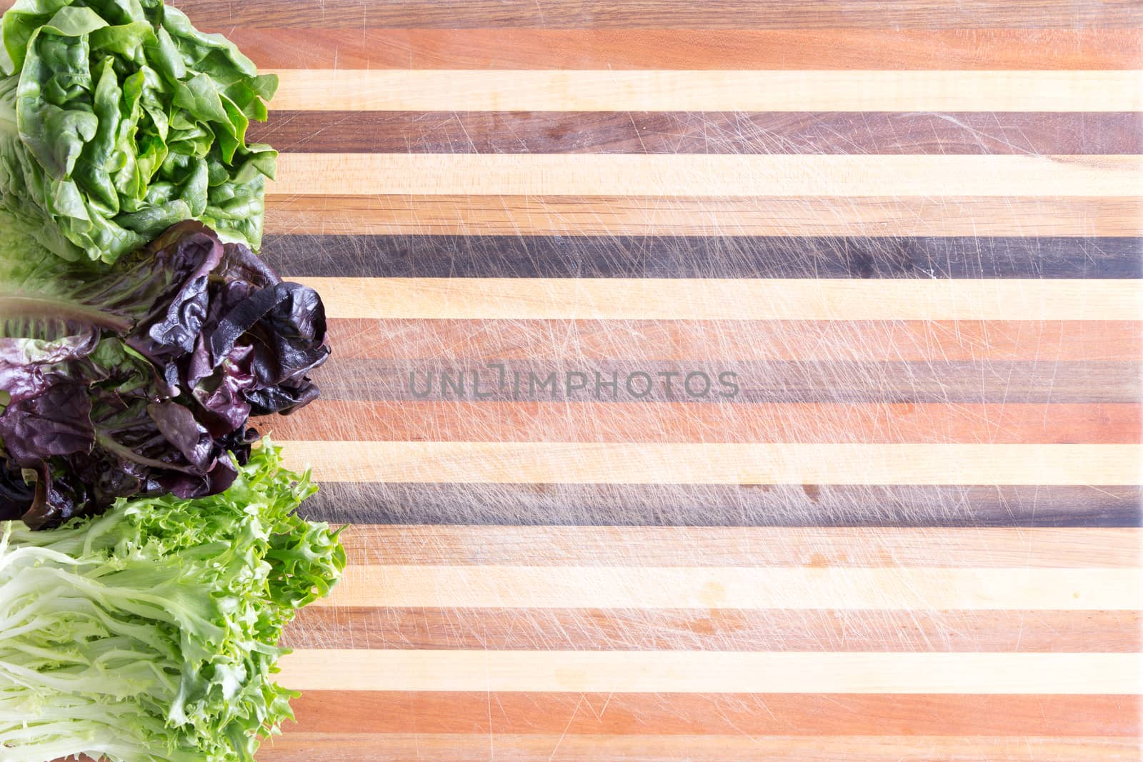 Fresh lettuce border with three cultivars on a decorative laminated wood chopping board with assorted colors of wood in a parallel stripe pattern with copy space, viewed from above