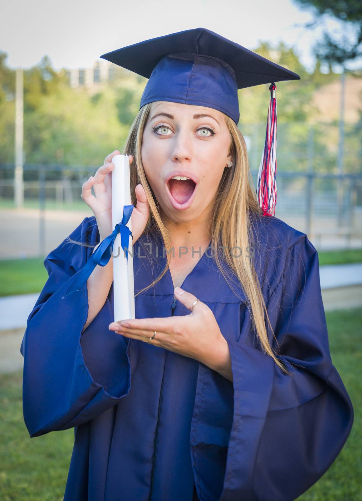 Excited and Expressive Young Woman Holding Diploma in Cap and Gown Outdoors.