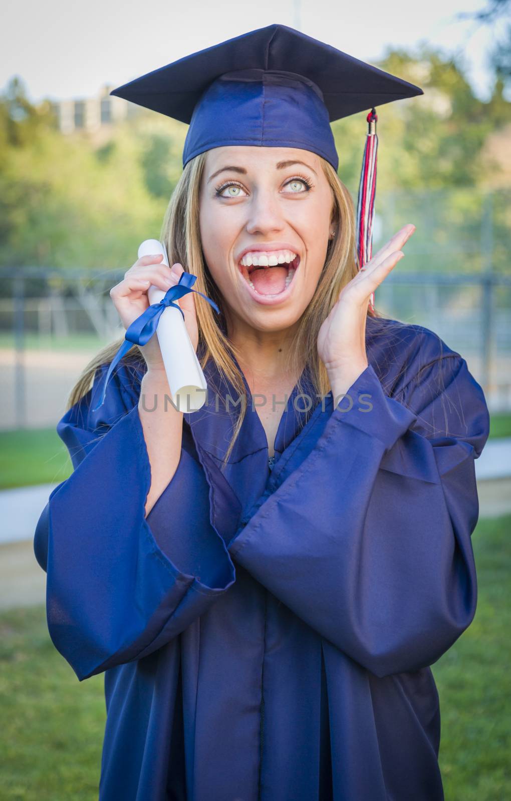 Excited and Expressive Young Woman Holding Diploma in Cap and Gown Outdoors.