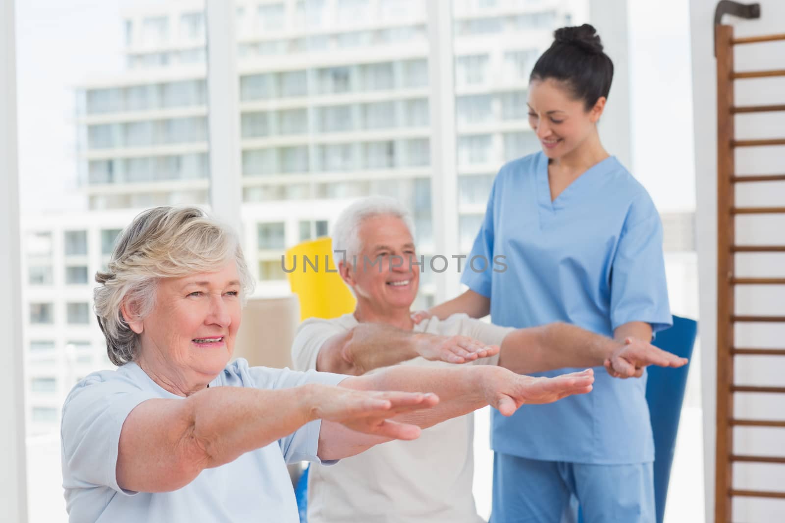Happy female instructor assisting senior couple to exercise in gym