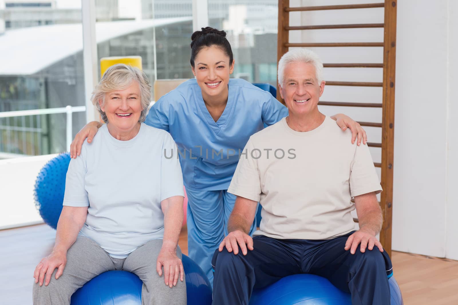 Portrait of happy female trainer with arms around senior couple in gym