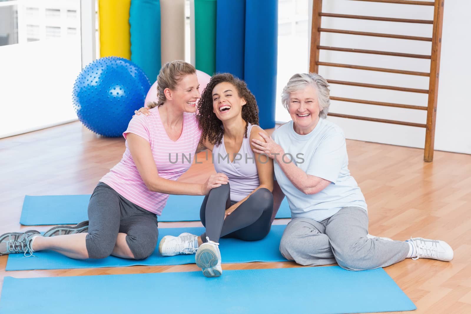 Playful friends sitting on exercise mat in gym by Wavebreakmedia
