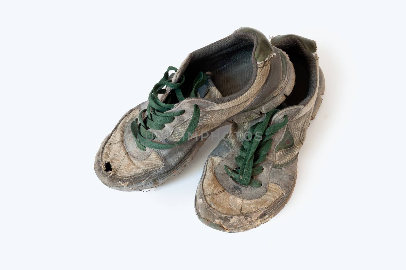 Old discarded sneakers with green shoelaces photographed against a white background