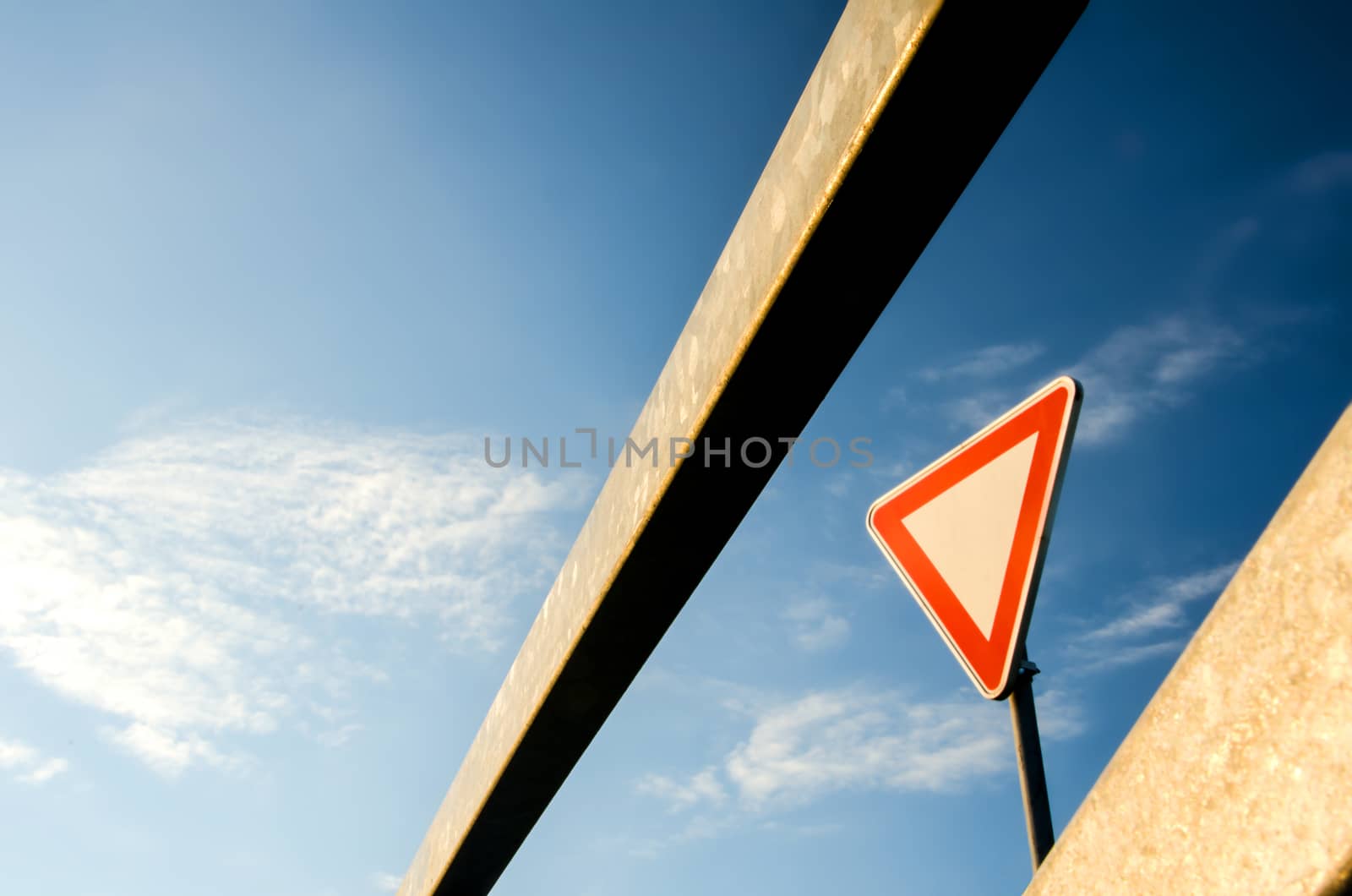 Bar and triangle traffic sign against blue sky.