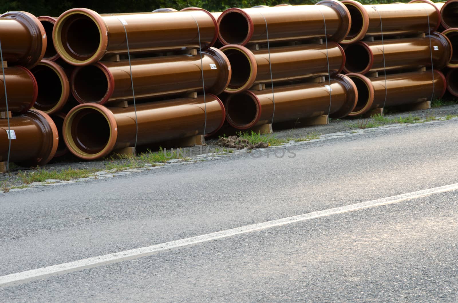 Stacks of pipes next to asphalt road. 