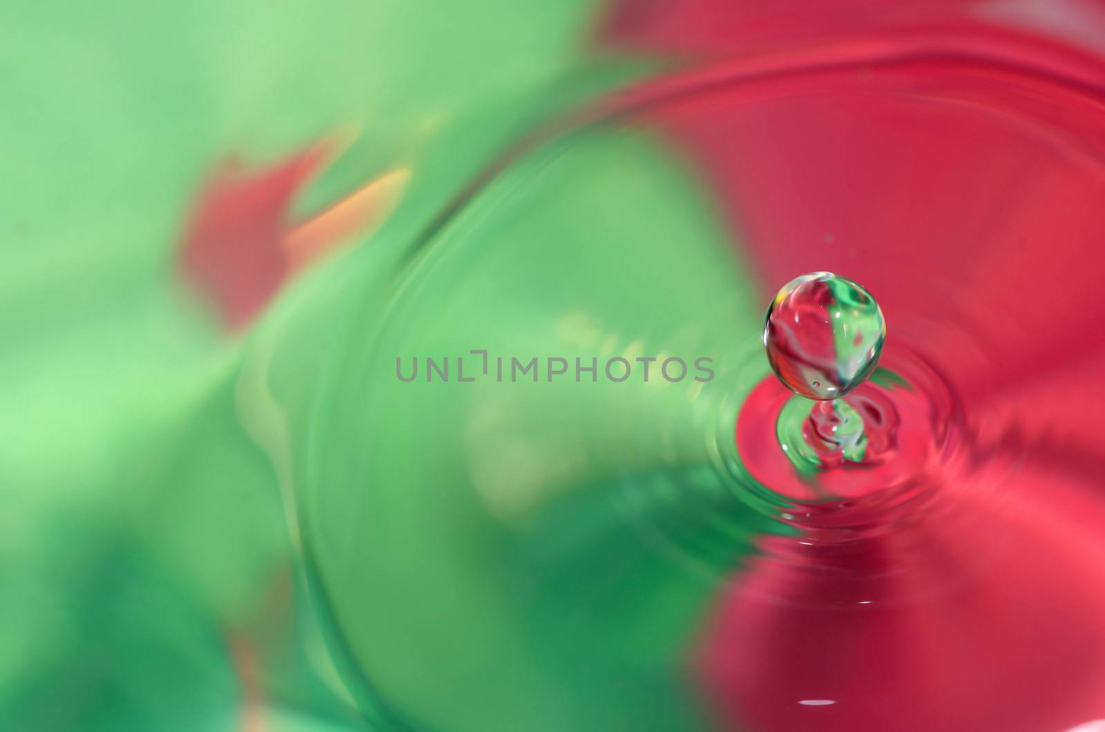 Water drop is falling into the water, red green background. 