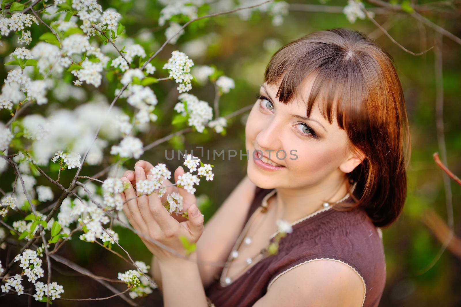 outdoor portrait of a beautiful brunette woman in blue dress among blossom apple trees 