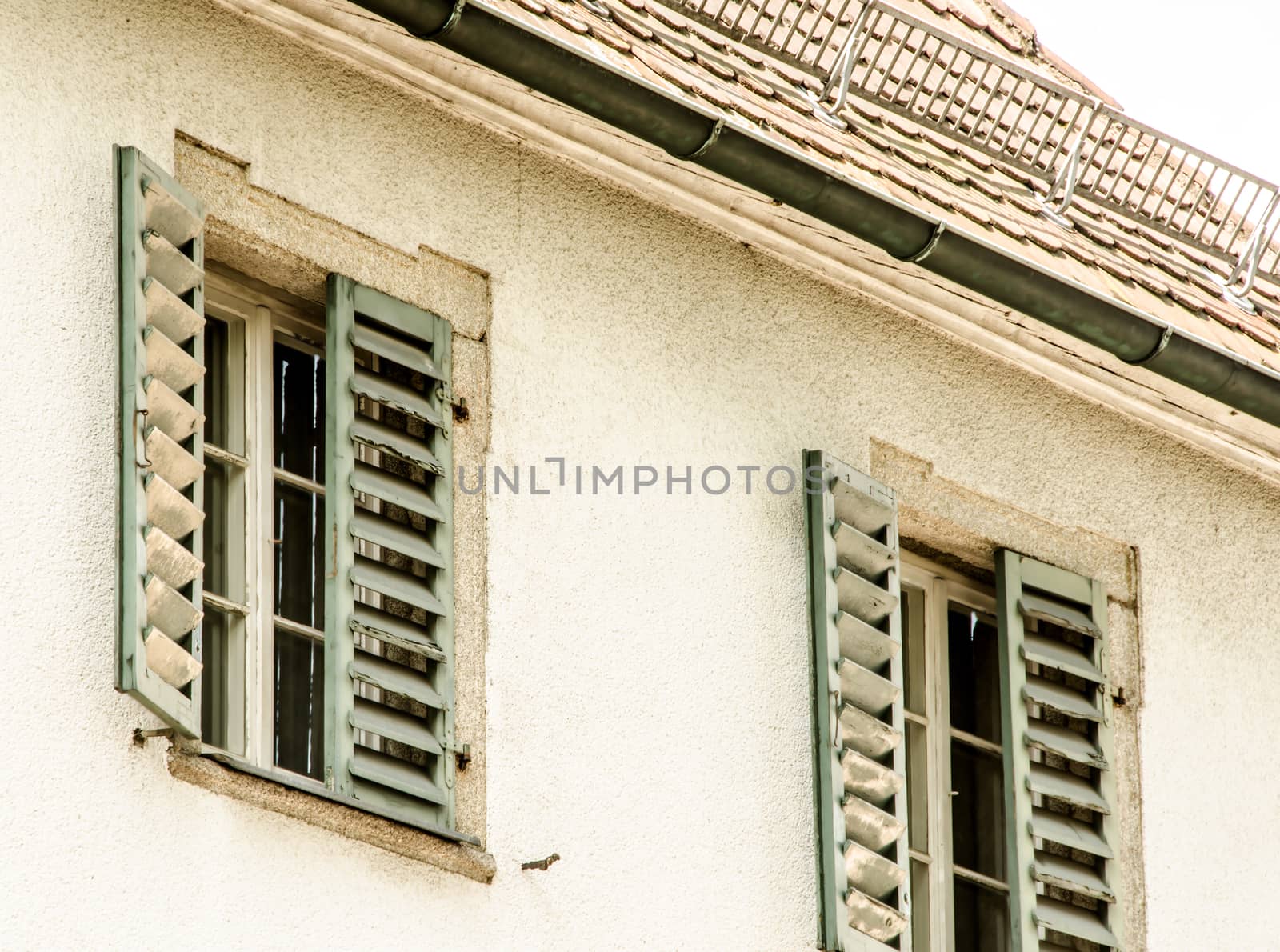 Two windows with green window shutters and old roof.
