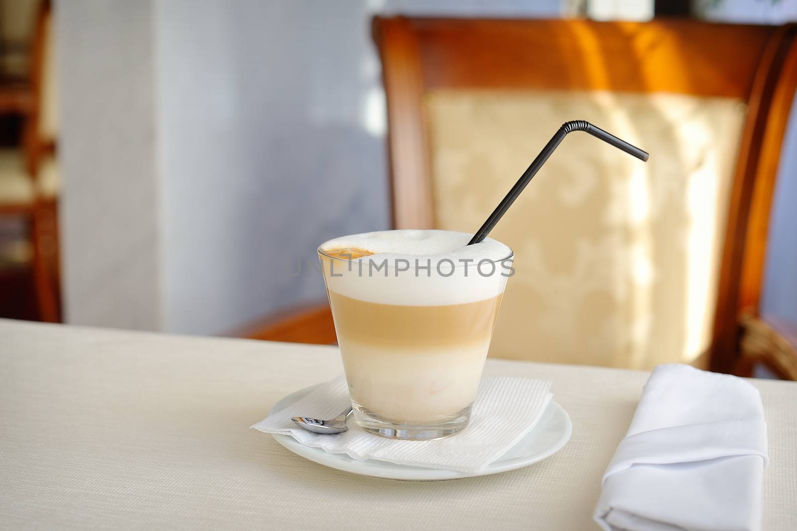 cup of latte with straw on a table in a restaurant.