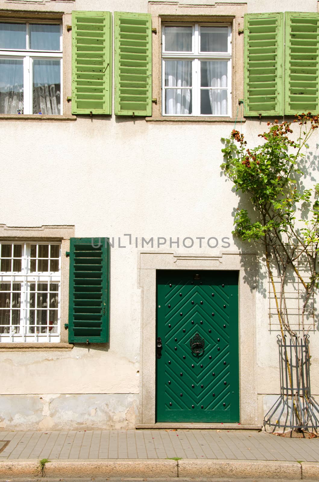 Old german house with green door and shutters, sidewalk in the front. 