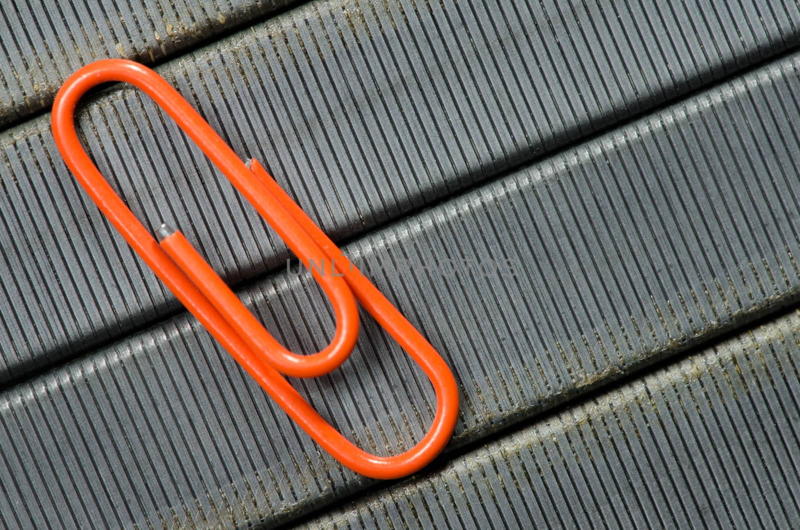 Orange paper clip on staple wire background as symbol of solitude. 