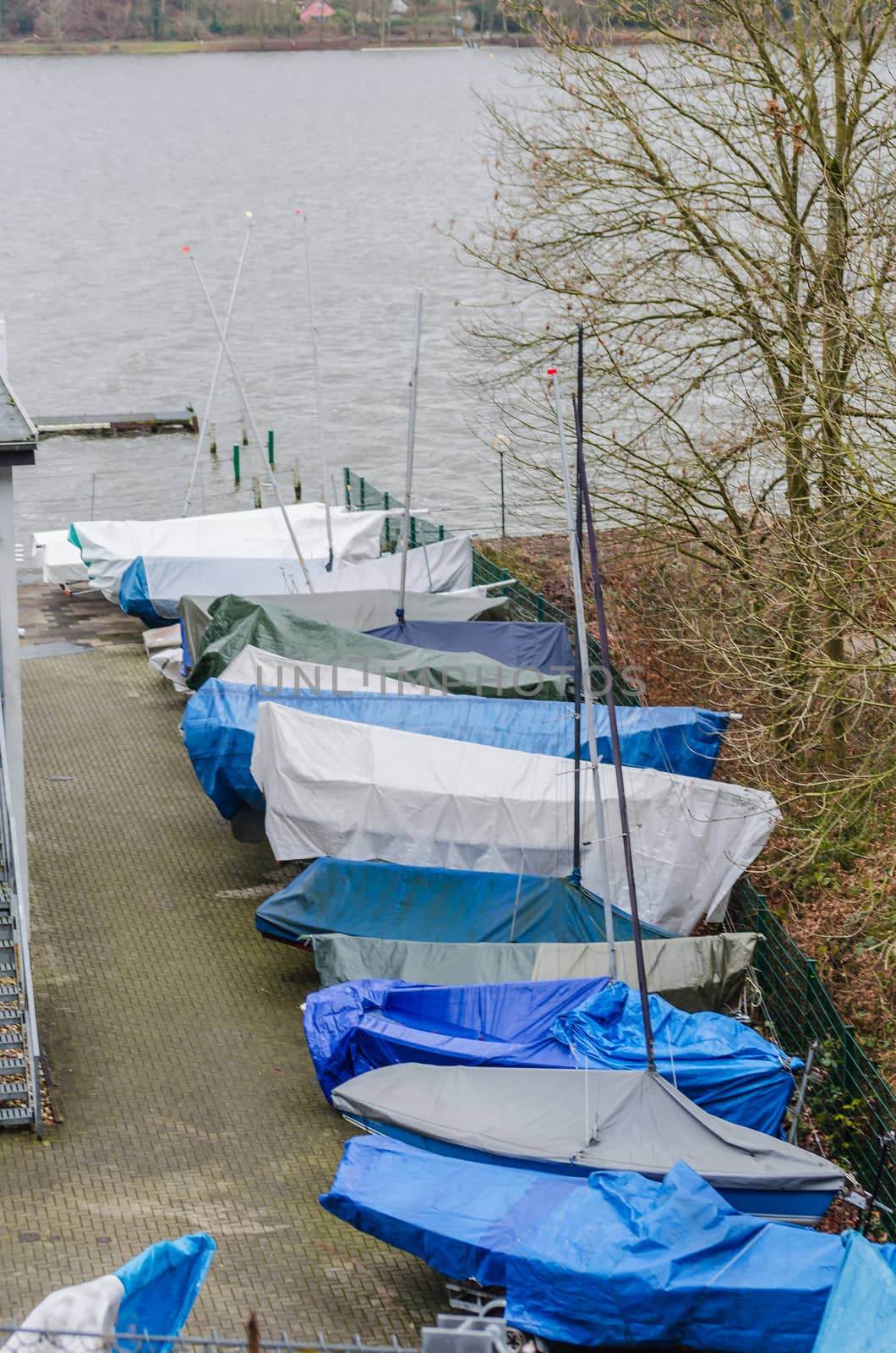 Small sailboats covered with a blue tarp for the winter on land.