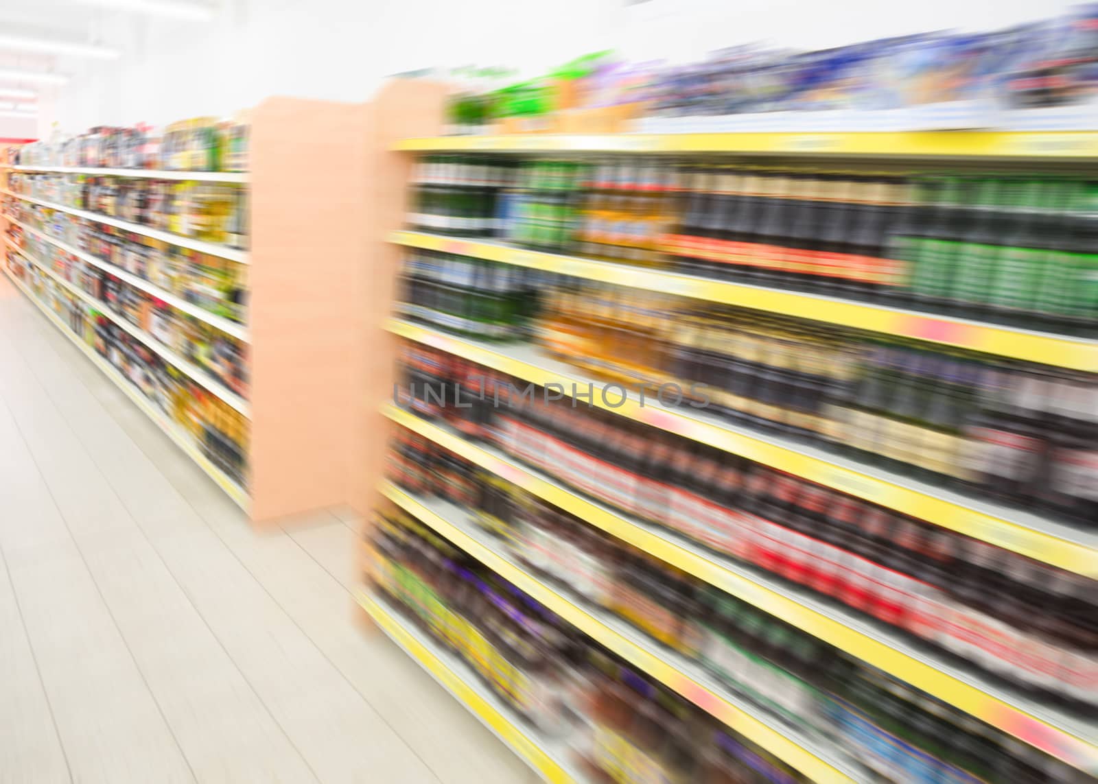 Long shelves with beverages bottles in big grocery food store in supermarket. Filtered stock photo blurred in motion.