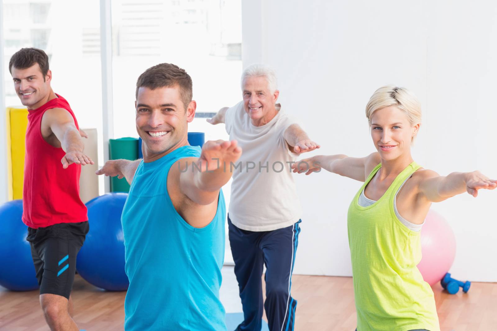 Happy people doing warrior pose in yoga class by Wavebreakmedia