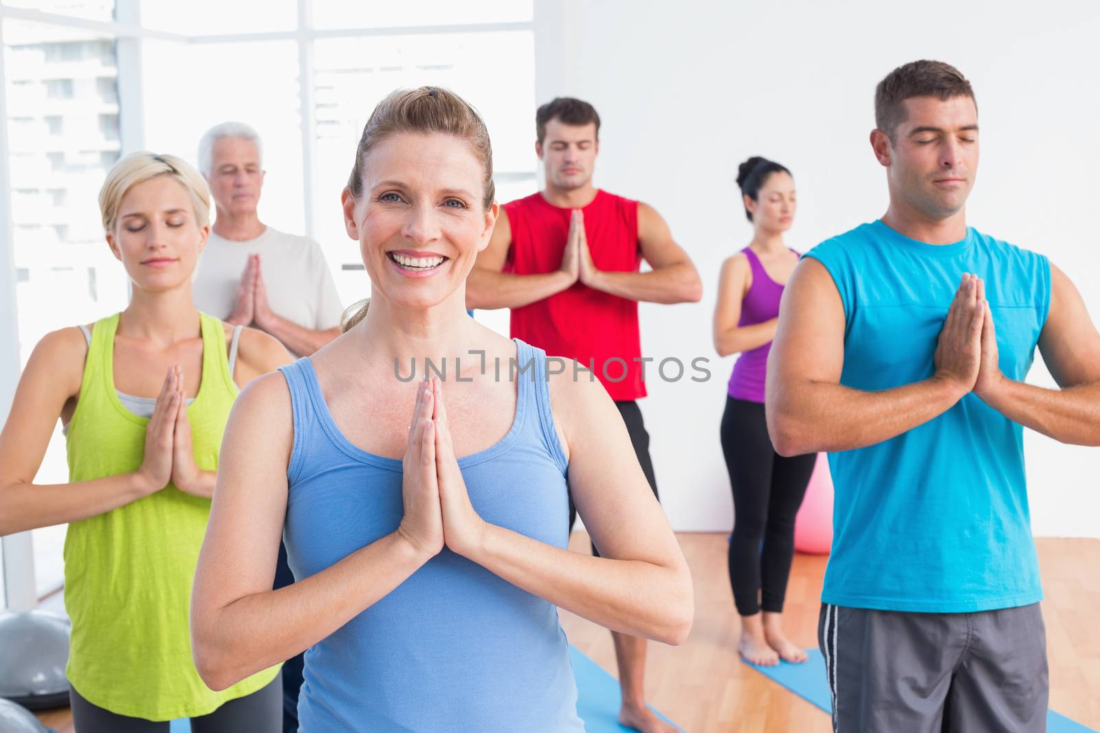Happy woman with friends meditating with hands joined in yoga class