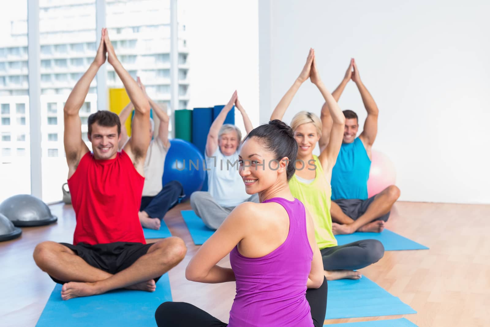 Portrait of female instructor with class practicing yoga in fitness studio