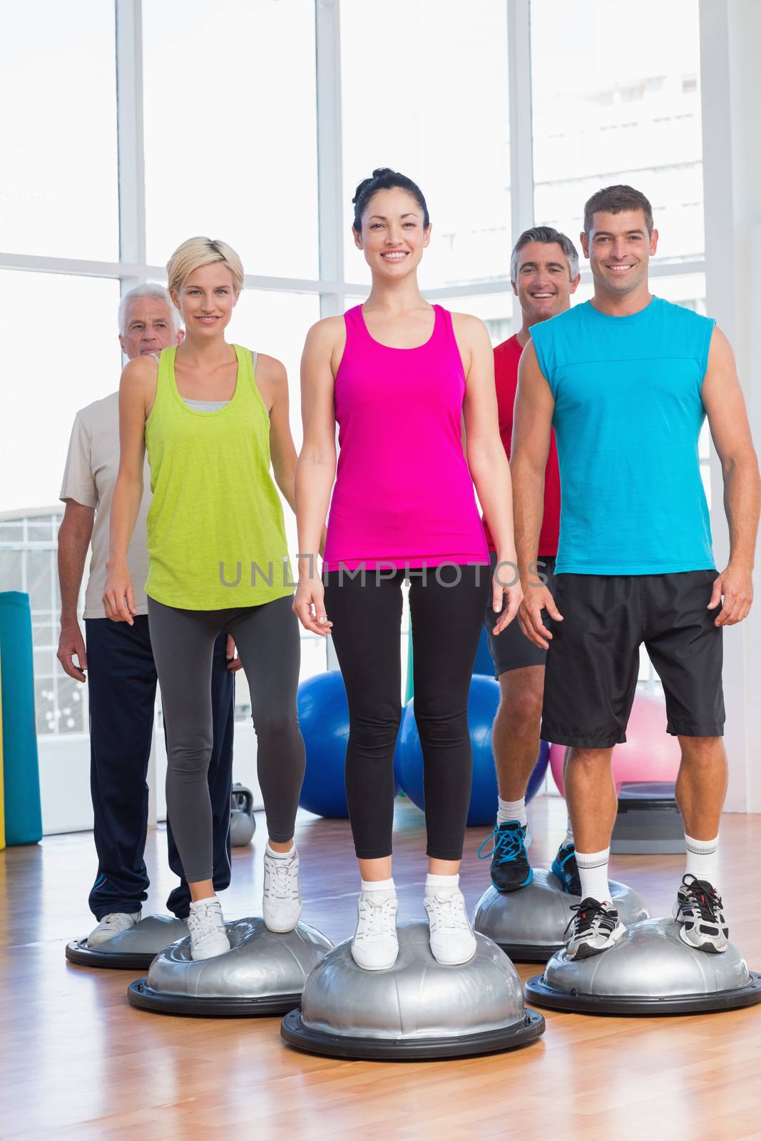Full length portrait of people standing on balance balls in gym