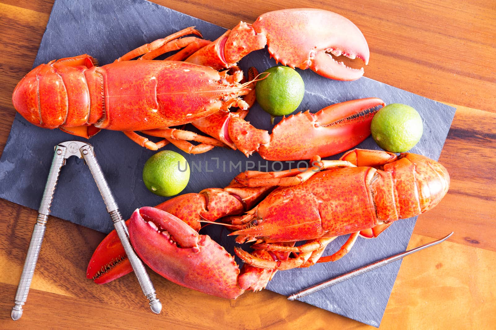 Close up Cooked Red Lobsters Duo on a Gray Cutting Board with Lime and Cracking Tool, on Top of a Wooden Table.