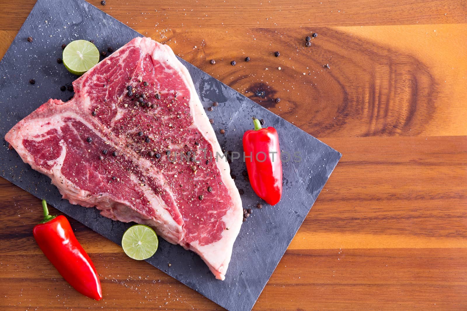 Close up T-Bone Steak Meat Marinated with Whole Black Peppercorn on a Gray Cutting Board with Lime and Cayenne Pepper,Prepared on a Wooden Table.