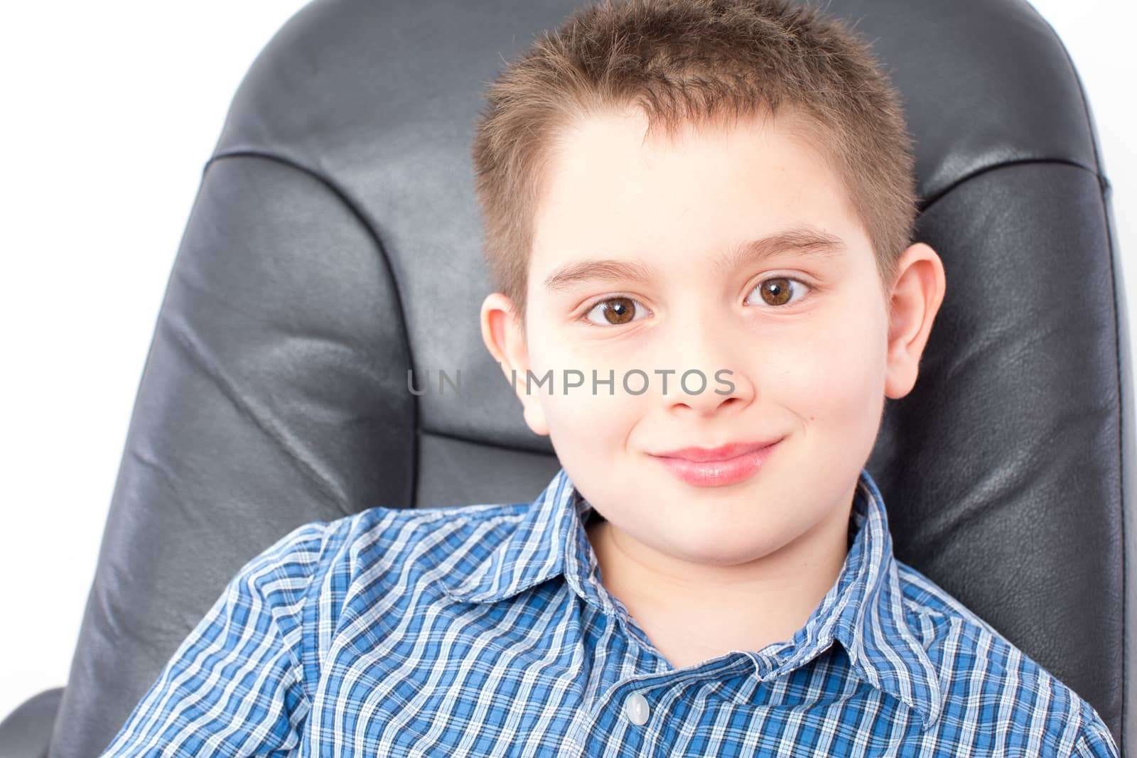 Close up Smiling Cute American Boy Sitting on a Black Office Chair, Looking at the Camera, on a White Background.