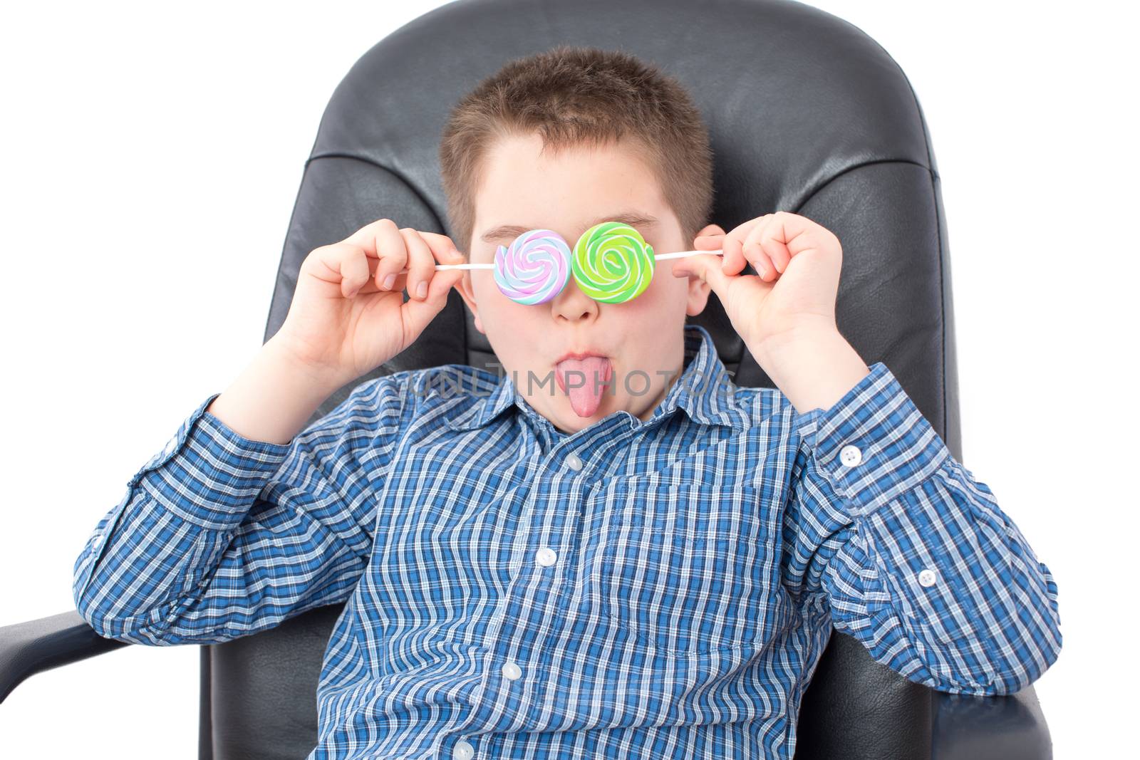 Close up Funny White Boy in Checkered Shirt, Sitting on an Office Chair and Holding Lollipops Over his Two Eyes with Tongue Out. Isolated on White.