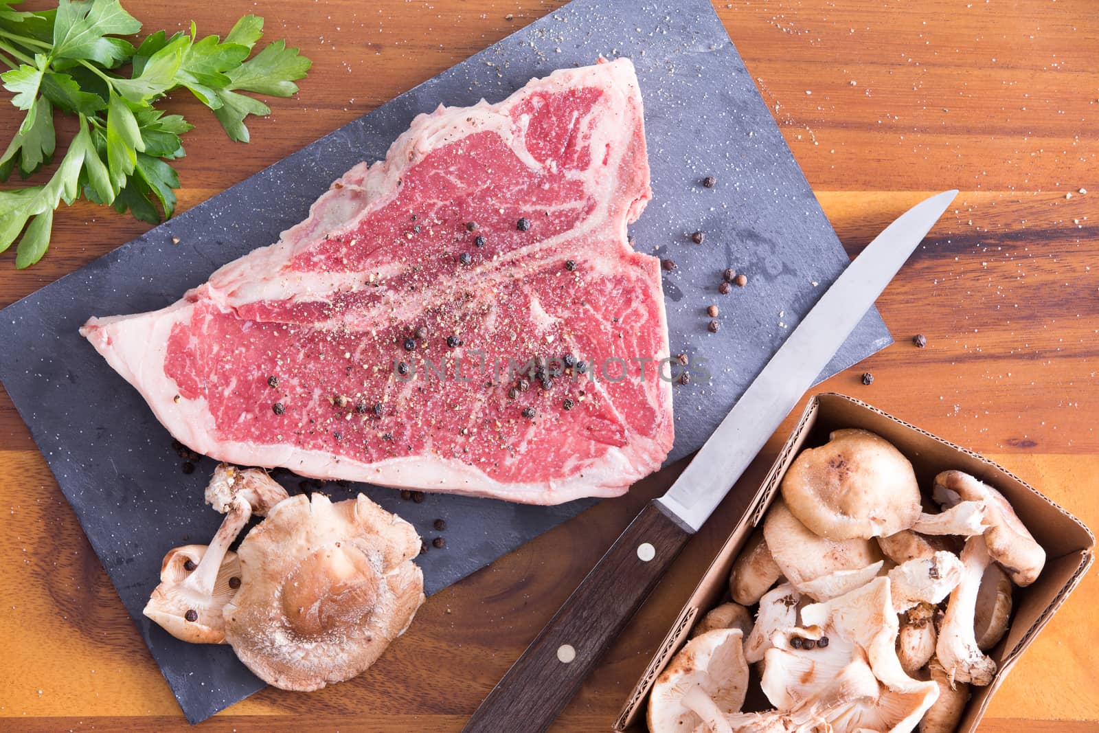 Ready to Cook T-Bone Steak Marinated with Black Peppercorn on a Cutting Board, Placed on Top of a Wooden Table with Parsley and Punnet Golden Oak Shiitake Mushrooms